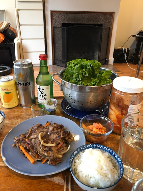 Korean BBQ spread: glazed rib eye with carrots and onion, rice, kimchi, lettuce wraps, soju and beer on a wooden table